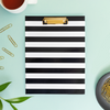 black and white stripe clipfolio on a mint green background, tea cup, gold paperclips, black dish, green leaves