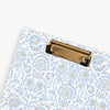 close up of repeated classic light blue and gold pattern clipfolio with gold clip on a cream background
