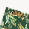 close up of green and gold palm leaves pattern clipfolio with gold clip on a dark green background