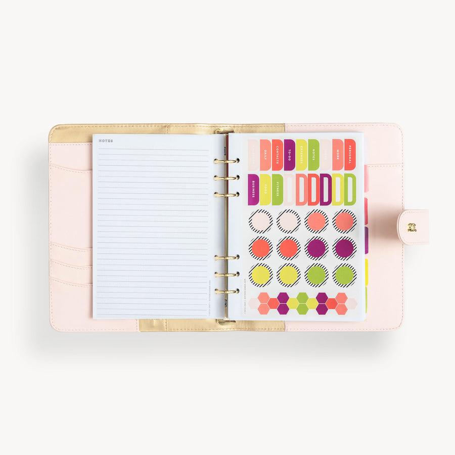Blush binder open to show blush and gold interior with pockets, notes page and colorful stickers