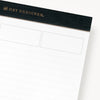 Planning pad with black and gold trim with lined notepad shown in close up