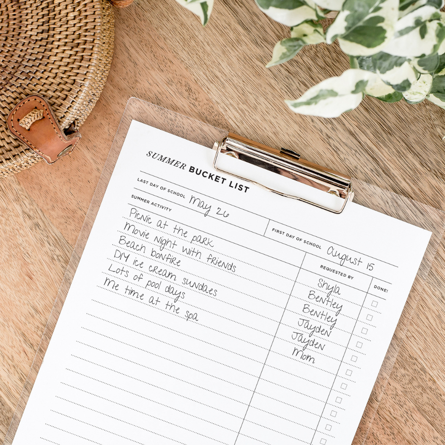 summer bucket list printable, written on page attached to clipboard, plant, wood desk, wicker purse
