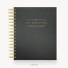 A black textured spiral-bound planner cover with gold lettering reading 'DAY DESIGNER' and gold spiral binding along the left edge, shown on a light gray background with the word 'COVER' below.