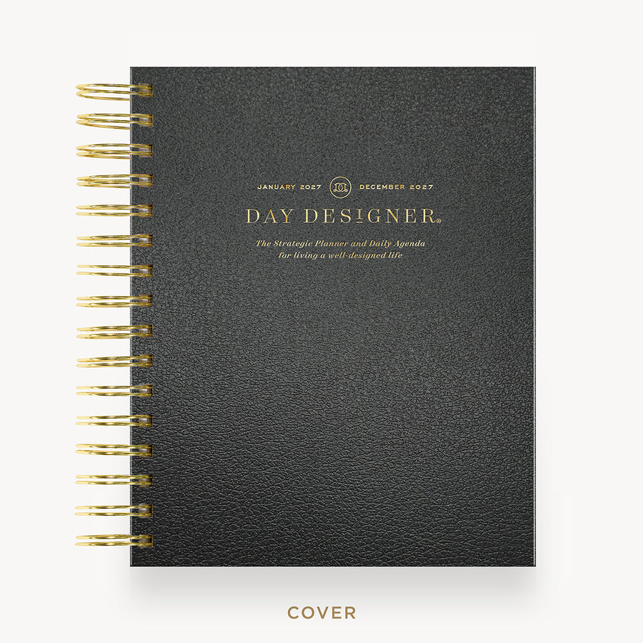 A black textured spiral-bound planner cover with gold lettering reading 'DAY DESIGNER' and gold spiral binding along the left edge, shown on a light gray background with the word 'COVER' below.