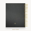 A black textured leather planner or notebook shown from the back, with gold spiral binding along the right edge and a small gold circular logo near the bottom. The words 'BACK COVER' appear below on a light gray background.