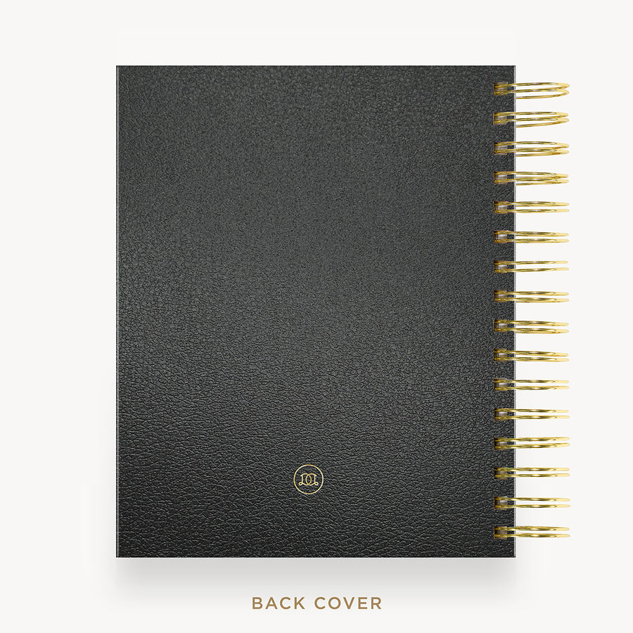 A black textured leather planner or notebook shown from the back, with gold spiral binding along the right edge and a small gold circular logo near the bottom. The words 'BACK COVER' appear below on a light gray background.