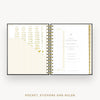 An open spiral-bound planner or pocket organizer shown from above on a light gray background. The pages are white with gold text, gold measurement rulers, and gold striped accents.