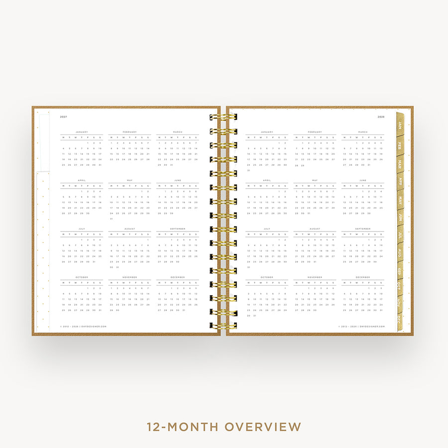 An open spiral-bound planner showing a 12-month calendar overview on white pages, with a gold wire binding and gold page edges, centered on a light gray background. Text below reads '12-MONTH OVERVIEW'.