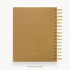 A tan textured spiral-bound notebook shown from the back, with gold-toned wire binding along the right edge and the words 'BACK COVER' printed below on a light gray background.