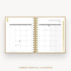 An open spiral-bound monthly calendar planner shown from above on a light gray background. The pages are white with gray grid lines and headers, and the center binding is gold.