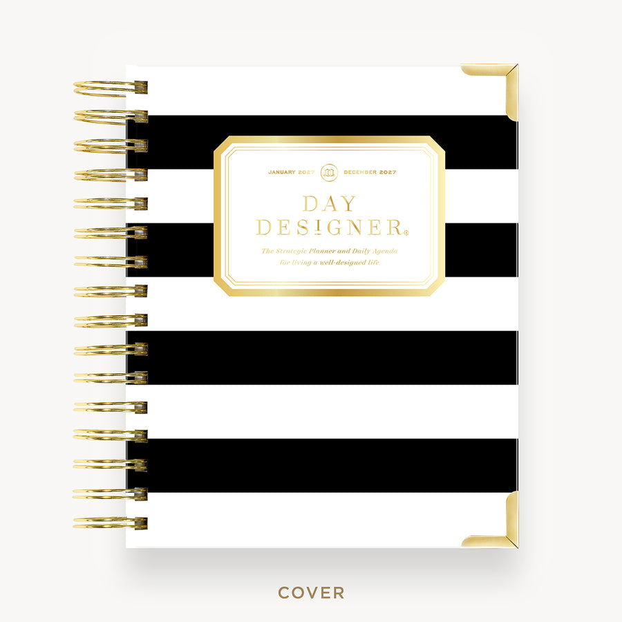 A spiral-bound planner or journal cover shown from the front, featuring bold horizontal black and white stripes with a central gold-bordered label that reads 'DAY DESIGNER.' The cover is photographed on a clean white background with gold-toned spiral binding and small gold corner accents.