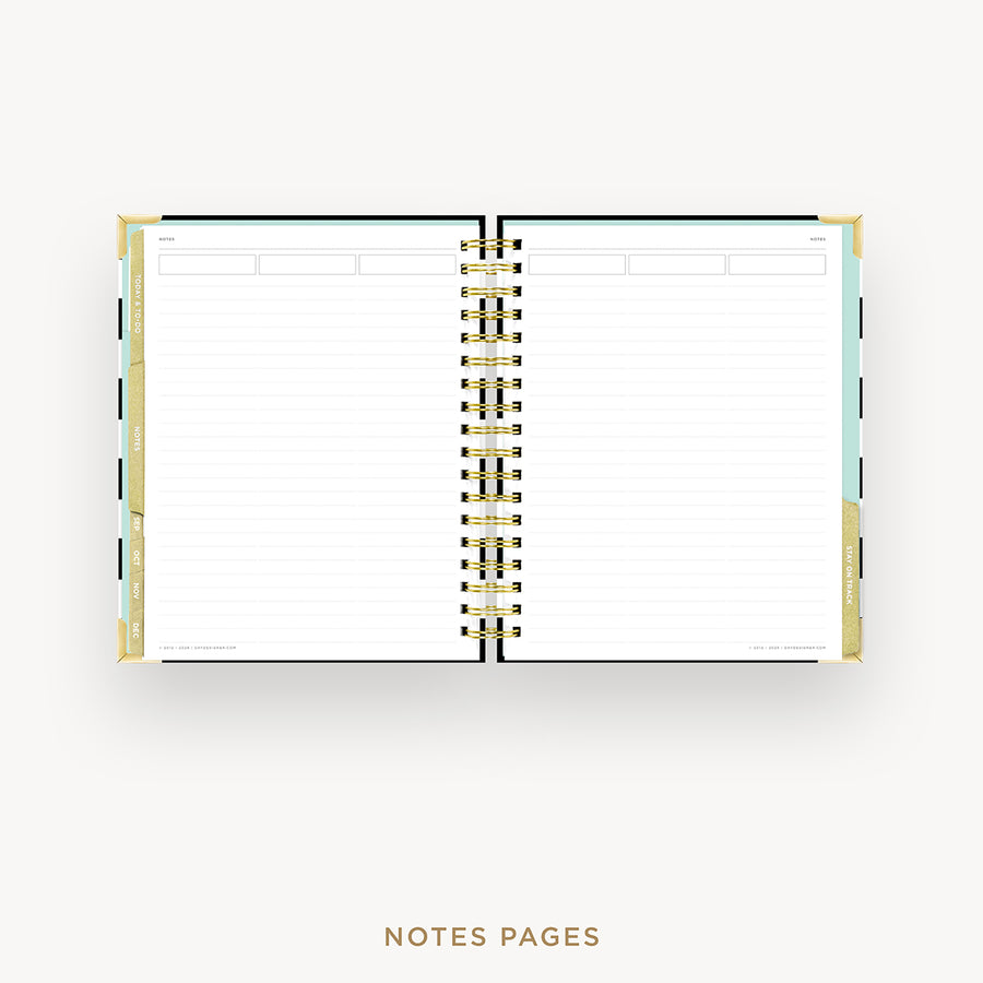 An open spiral-bound planner or notebook with lined white pages, shown on a light gray background. The cover edges are pale blue and beige, and the center binding is gold.