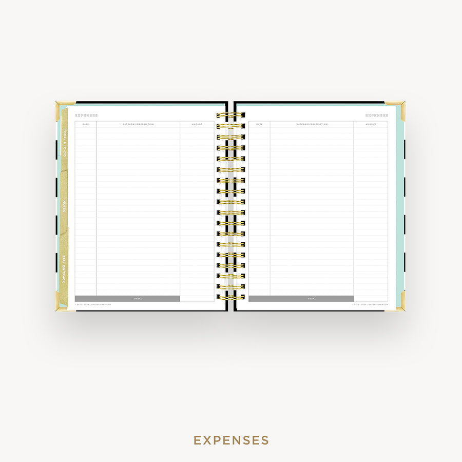 An open spiral-bound planner showing the Expenses page with lined columns, photographed from above on a light gray background. The cover has a gold-toned edge, and the word EXPENSES appears below the planner.