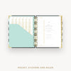 An open spiral-bound planner or organizer shown from above on a light gray background. The pages are white with gold typography and a large pale mint pocket on the left page.