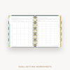 An open spiral-bound planner or notebook showing goal-setting worksheet pages on the left and a monthly calendar grid on the right, with decorative gold rings and a light blue accent tab on a white background. Text below reads 'GOAL-SETTING WORKSHEETS'.
