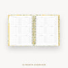 An open spiral-bound 12-month overview planner shown from above on a light gray background, with a floral-patterned gold and white cover and gold wire binding.