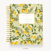 A spiral-bound daily planner cover shown from the front on a light gray background. The cover features a botanical lemon pattern with yellow lemons, green leaves, white flowers, and small blue berries on a pale sage green base.