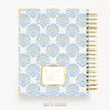 A spiral-bound planner or notebook shown from the back cover, featuring a repeating light blue and gold ornamental pattern on a white background, with a gold spiral binding and a small gold-bordered label area near the lower center.