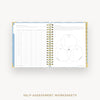 An open spiral-bound workbook showing self-assessment worksheet pages with tables and a Venn diagram, photographed on a light gray background with the text 'SELF-ASSESSMENT WORKSHEETS' below.