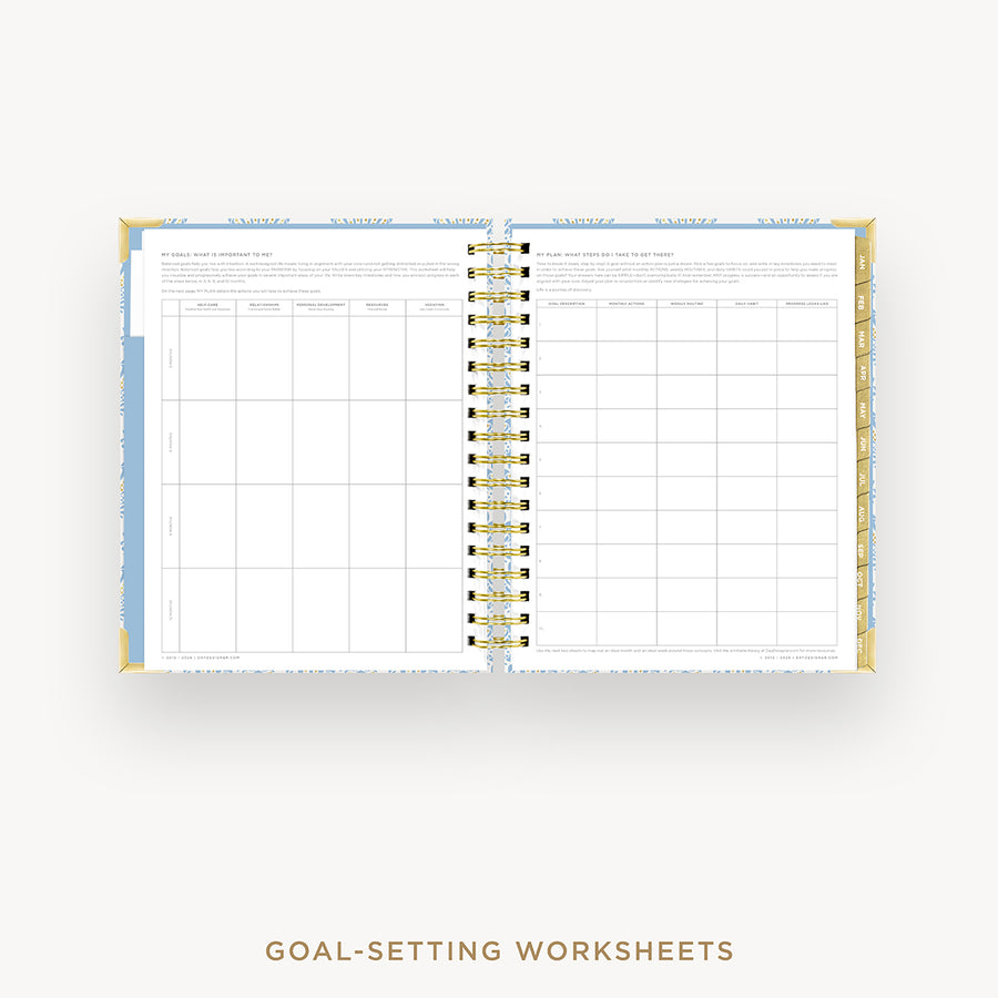 An open spiral-bound planner or notebook showing goal-setting worksheets on the pages, with a gold-toned ring binder and decorative gold and blue accents on the cover, photographed on a light gray background. Text below reads 'GOAL-SETTING WORKSHEETS'.
