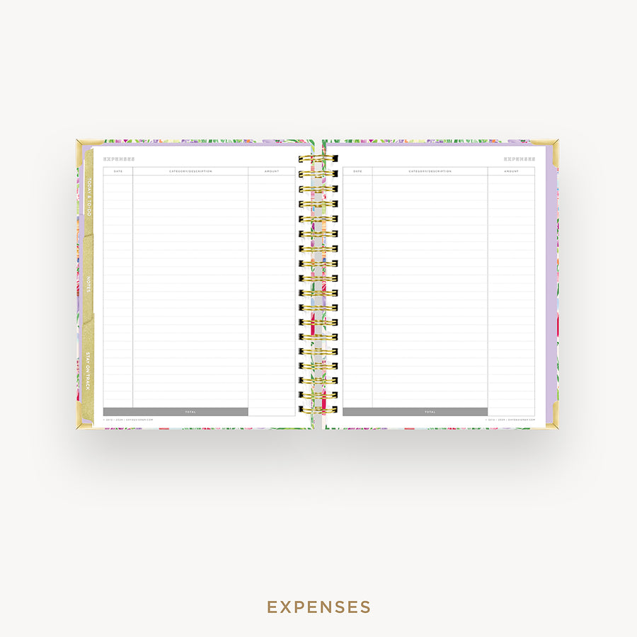 An open spiral-bound planner showing a clean expenses page with lined columns, photographed on a light gray background. The cover has a subtle pastel floral pattern, and the word EXPENSES appears below the product.