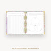 An open spiral-bound planner or notebook showing self-assessment worksheet pages, with a floral-patterned cover and gold-toned spiral rings, on a light gray background. Text below reads 'SELF-ASSESSMENT WORKSHEETS'.