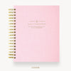 A light pink textured spiral notebook with gold wire binding and gold foil text on the cover reading 'DAY DESIGNER.' shown on a clean white background with the word 'COVER' below.