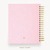A pink textured spiral notebook shown from the back cover, with gold wire binding along the right edge and a small circular logo near the bottom. The text 'BACK COVER' appears below on a light gray background.