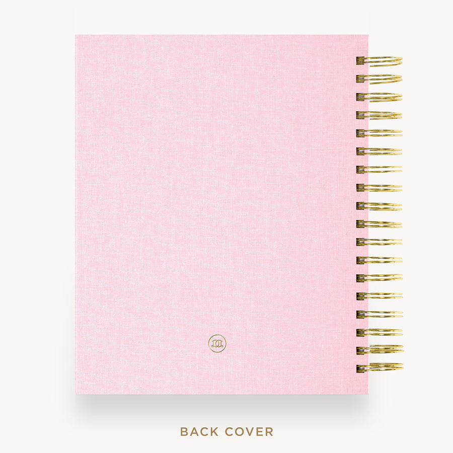 A pink textured spiral notebook shown from the back cover, with gold wire binding along the right edge and a small circular logo near the bottom. The text 'BACK COVER' appears below on a light gray background.