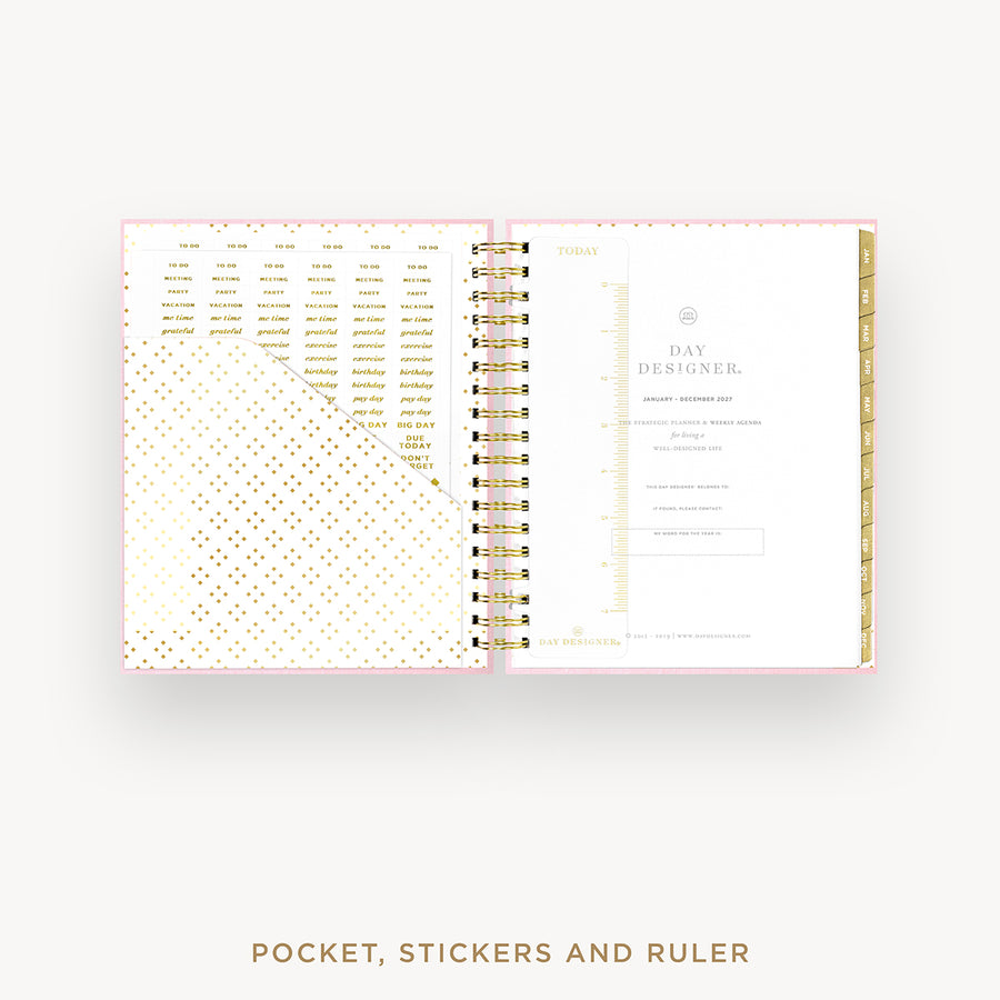 An open spiral-bound planner or pocket organizer shown on a light gray background, with gold foil dot patterns on the left page and a minimalist interior spread labeled 'Day Designer' on the right. Text below reads 'POCKET, STICKERS AND RULER'.
