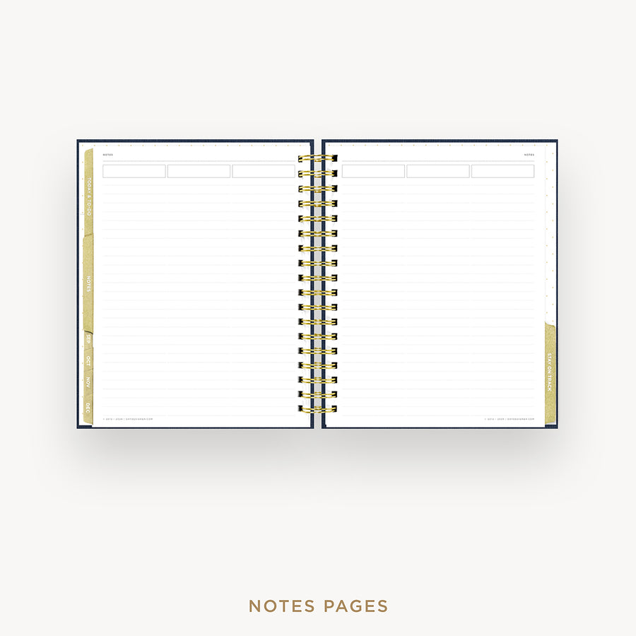 An open spiral-bound planner or notebook with lined pages, shown on a light gray background. The cover is dark navy blue, and the page edges and tab accents are a warm beige.