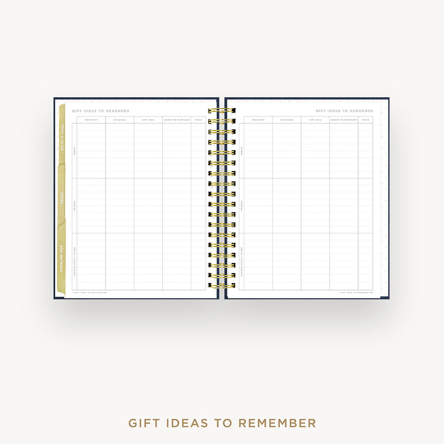 An open spiral-bound planner or notebook showing a gift ideas to remember grid page, photographed on a light gray background with the text 'GIFT IDEAS TO REMEMBER' below.