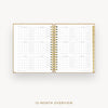 An open spiral-bound planner showing a 12-month overview calendar spread on white pages with gold-toned binding and gold page edges, centered on a light gray background with the text '12-MONTH OVERVIEW' below.