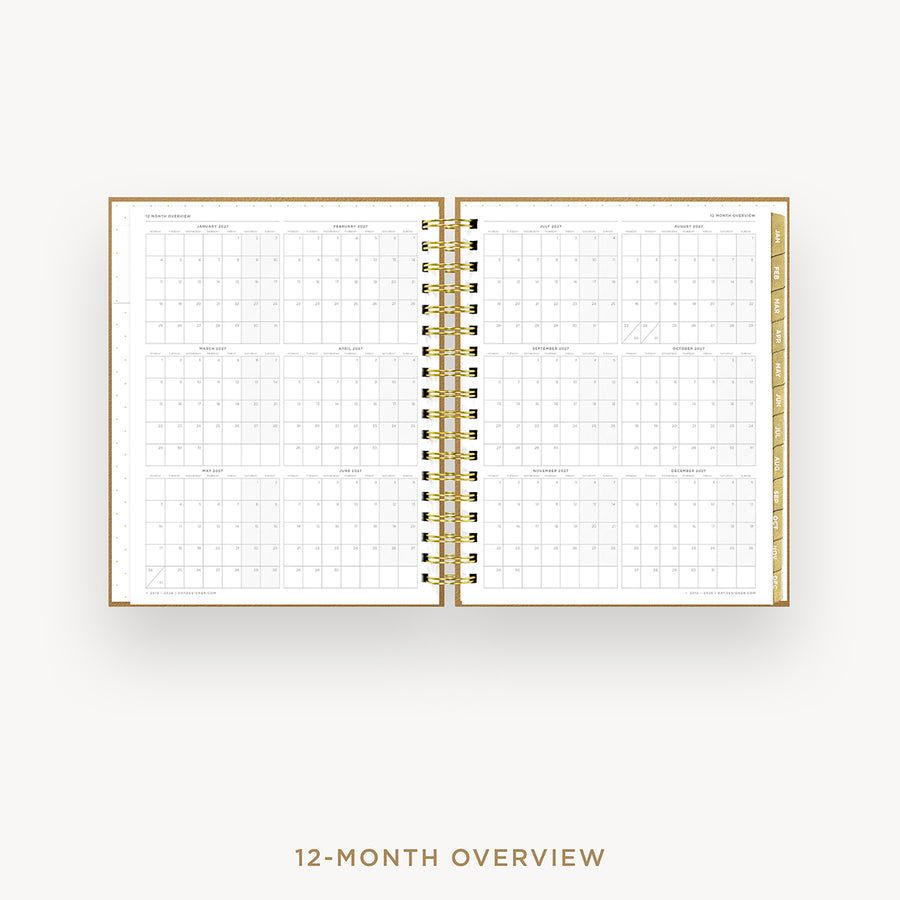 An open spiral-bound planner showing a 12-month overview calendar spread on white pages with gold-toned binding and gold page edges, centered on a light gray background with the text '12-MONTH OVERVIEW' below.