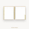 An open spiral-bound planner or notebook with lined notes pages, shown on a light gray background. The cover and binding are metallic gold, and the pages are white with faint horizontal lines.