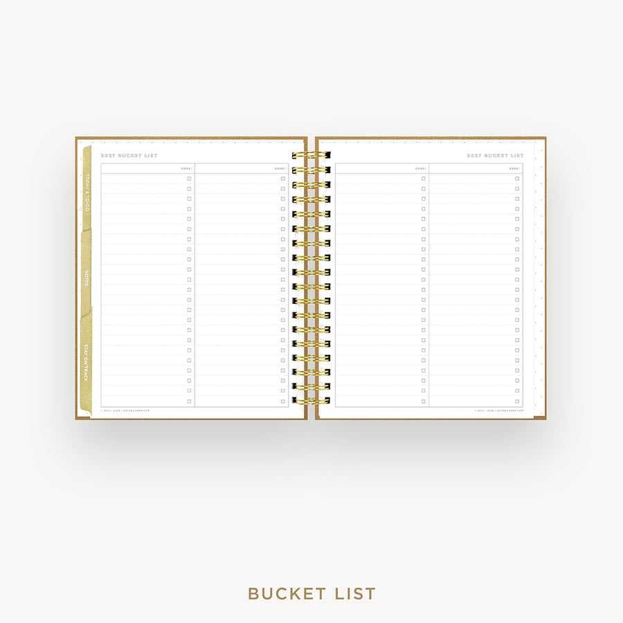 An open spiral-bound planner or notebook showing a gold-toned 'Bucket List' page spread on both sides, photographed on a clean white background with the words 'BUCKET LIST' centered below.