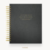 A black textured spiral-bound planner or agenda shown from the front on a light gray background. The cover has gold text reading 'DAY DESIGNER' and gold spiral binding along the left edge.