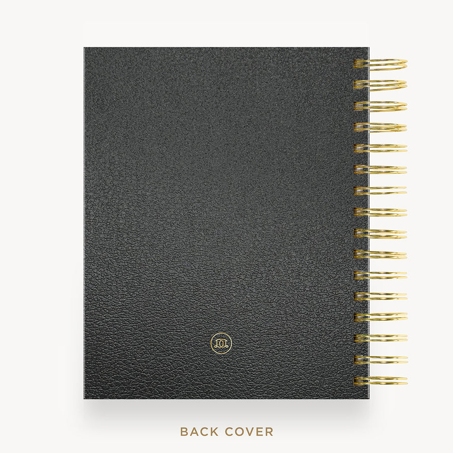 A black textured leather planner or notebook shown from the back, with gold spiral binding along the right edge and a small gold circular logo near the bottom. The text 'BACK COVER' appears below on a light gray background.