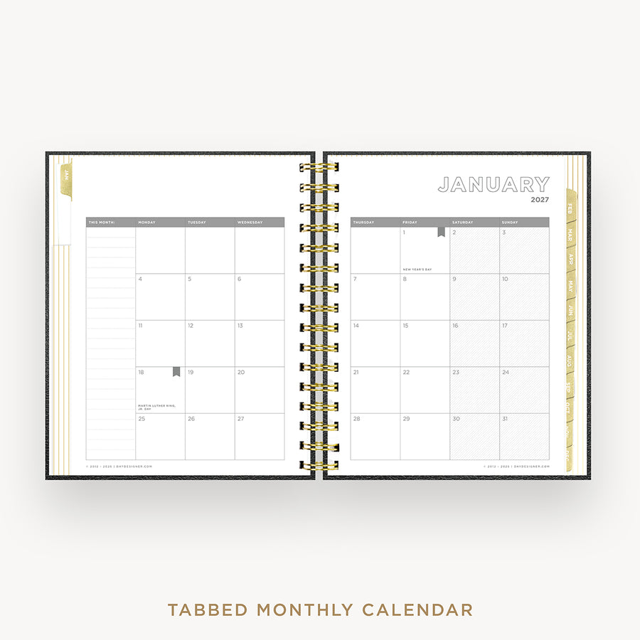 An open tabbed monthly calendar planner shown from above on a light gray background. The pages are white with gray grid headers and gold-toned spiral binding down the center.