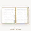 An open spiral-bound planner or calendar showing a 12-month overview layout on white pages, with a gold-toned ring binder and matching gold text below reading '12-MONTH OVERVIEW'.