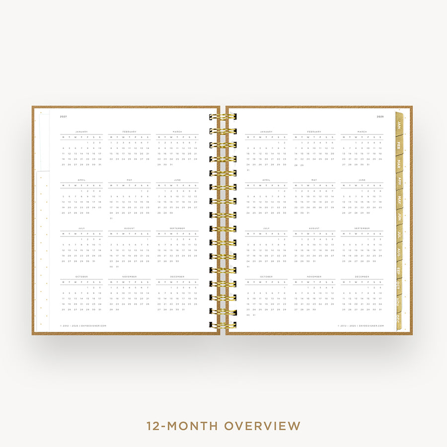 An open spiral-bound planner or calendar showing a 12-month overview layout on white pages, with a gold-toned ring binder and matching gold text below reading '12-MONTH OVERVIEW'.