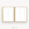 An open spiral-bound bucket list planner on a light gray background. The pages are white with gold lines and gold ring binder hardware, featuring lined sections with checkboxes labeled for daily, weekly, monthly, and yearly goals.