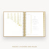 An open spiral-bound planner or pocket organizer shown on a light gray background, with gold-toned inner pages, stickers, and a ruler visible. Text below reads 'POCKET, STICKERS AND RULER'.