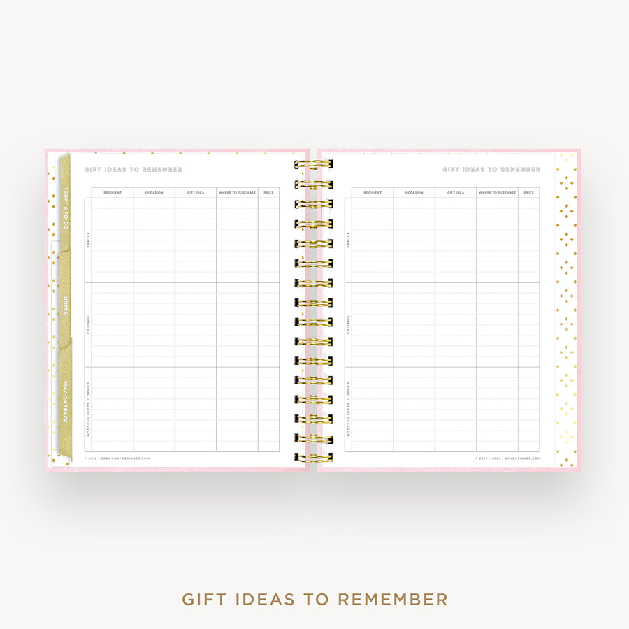 An open spiral-bound planner or notebook showing gift ideas to remember pages, with a pale pink border, gold rings, and a gold vertical accent strip on a light gray background. Text below reads 'GIFT IDEAS TO REMEMBER'.