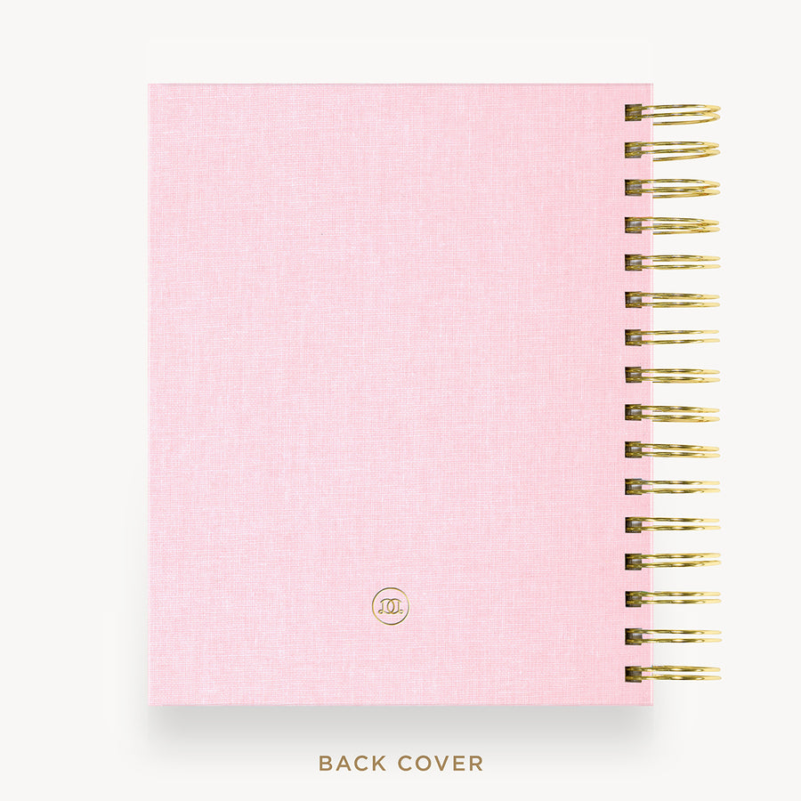 A light pink textured spiral notebook shown from the back, featuring a gold-tone spiral binding along the right edge and a small circular monogram logo near the bottom. The text 'BACK COVER' is printed below the notebook on a clean white background.