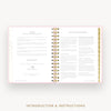 An open spiral-bound booklet or planner showing printed introduction and instructions pages, with a pink border, gold foil accents, and a light neutral background. The text at the bottom reads 'INTRODUCTION & INSTRUCTIONS'.