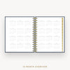 An open spiral-bound planner showing a 12-month calendar overview on white pages, with a navy blue cover edge and gold-toned spiral binding. The text '12-MONTH OVERVIEW' appears below on a light gray background.