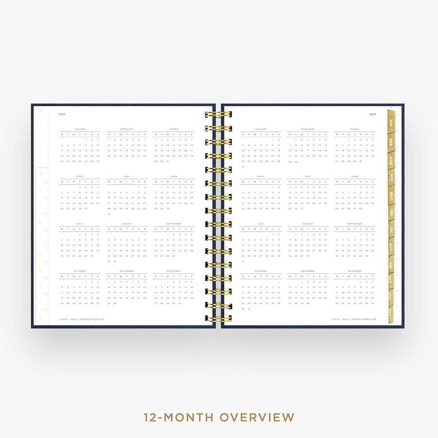 An open spiral-bound planner showing a 12-month calendar overview on white pages, with a navy blue cover edge and gold-toned spiral binding. The text '12-MONTH OVERVIEW' appears below on a light gray background.