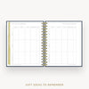 An open spiral-bound planner or notebook showing a gift ideas to remember page spread, with gold-toned wire binding and a gold vertical tab on the left page, set on a light gray background with the text 'GIFT IDEAS TO REMEMBER' below.