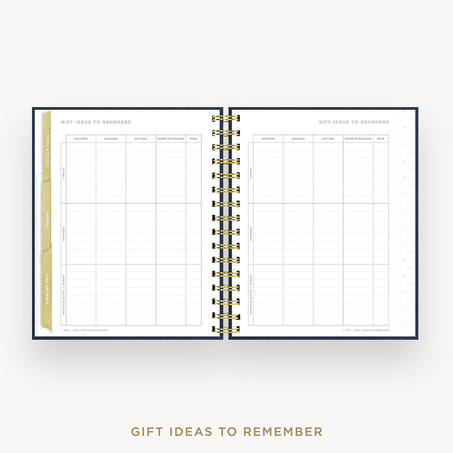 An open spiral-bound planner or notebook showing a gift ideas to remember page spread, with gold-toned wire binding and a gold vertical tab on the left page, set on a light gray background with the text 'GIFT IDEAS TO REMEMBER' below.